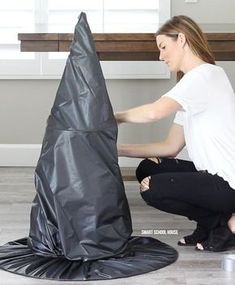 a woman kneeling on the floor next to a black piece of art that looks like a cone