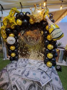 a table topped with lots of money under a tent covered in gold and black balloons