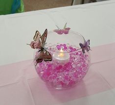 a glass bowl filled with lots of pink beads and butterflies on top of a table