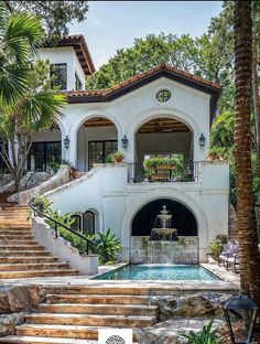 a large white house with stairs leading up to the front door and water fountain in the middle