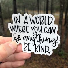 someone holding up a sticker that says in a world where you can be anything kind