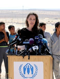 a woman standing at a podium with microphones in front of her and people behind her