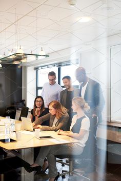 a group of people standing around a table with laptops and papers in front of them