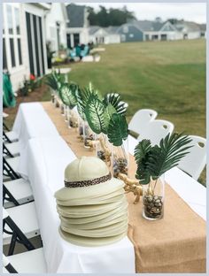 a long table topped with lots of white plates and vases filled with palm leaves