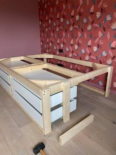 an unfinished bed frame with drawers and tools on the floor in front of a floral wallpaper