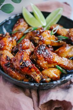 chicken wings with sauce and herbs in a black bowl on a pink cloth next to a green plant