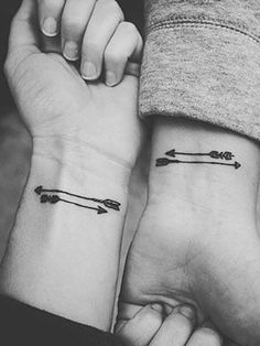 two people holding hands with tattoos on their wrist and one has an arrow in the middle