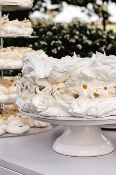 a cake with white frosting and daisies on it sitting on a table in front of other cakes