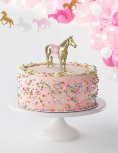 a birthday cake with pink frosting and gold horse figurines on top, surrounded by balloons