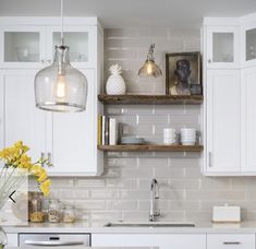 a kitchen with white cabinets and yellow flowers on the counter top in front of two hanging lights