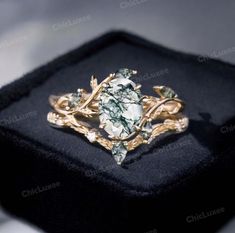 a gold ring with green and white stones in it's center on a black velvet box