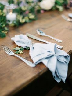 the table is set with silverware, napkins and greenery on top of it