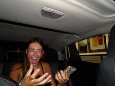 a woman sitting in the back seat of a car with her mouth open and holding a cell phone