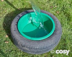 a green plastic bowl filled with water on top of a grass covered field next to a tire