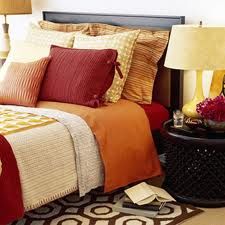 a bed with orange and red pillows on top of it next to a table with two lamps