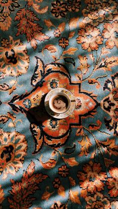 a coffee cup sitting on top of a blue and orange rug with an ornate design