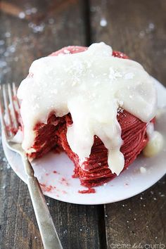 a piece of red velvet cake with white icing on a plate next to a fork