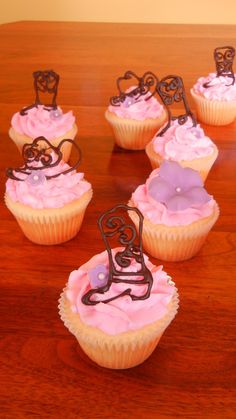 several cupcakes with pink frosting and chocolate decorations on top of a wooden table