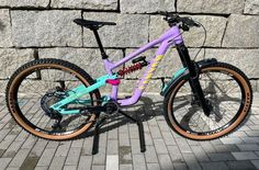 a purple and blue bike parked next to a stone wall