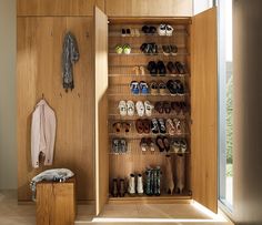 a wooden closet filled with lots of shoes next to a wall mounted coat rack and window