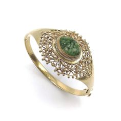 This is part of Chairish’s Fine Jewelry assortment.  This elegant bracelet is made of 14k gold and decorated with a central reticulated piece of green jade. The centre jade piece protrudes about a 1/4 of an inch from the gold setting and is carved with flower patterns. A lovely ring of seed pearls decorates the gold setting around the oval jade stone. From the central jade, as if emitting sinuous line-work, the gold work has a woven lace-like gold organic pattern detailed with beads of gold. The Green Cabochon Bracelet For Formal Occasions, Green Cabochon Bracelets For Formal Occasions, Elegant Green Cabochon Bracelets, Formal Green Cabochon Bracelets, Formal Green Cabochon Bracelet, Green Gemstone Gold Bracelet, Heirloom Jade Jewelry In Green, Heirloom Green Jade Jewelry, Elegant Oval Green Bangle