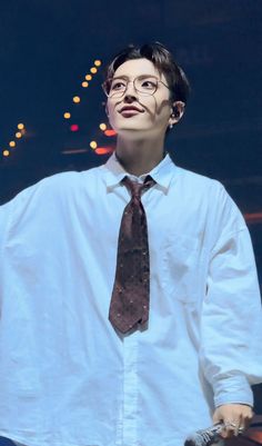 a man wearing glasses and a tie standing in front of a stage with his hands on his hips