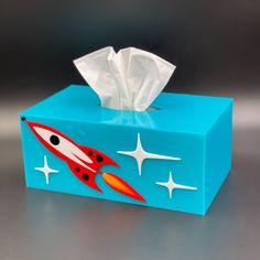 a blue tissue box with a rocket ship on it and stars painted on the side