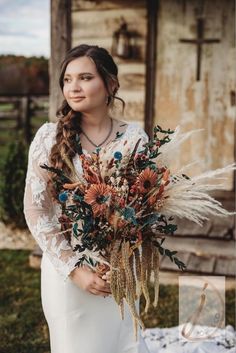 a woman holding a bouquet of flowers in front of an old building with grass and feathers on it