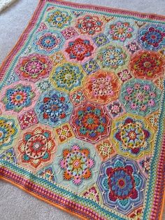 a colorful crocheted blanket is laying on the floor next to a white rug