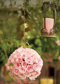 pink roses are hanging from a chandelier with a candle in the center and some greenery behind it