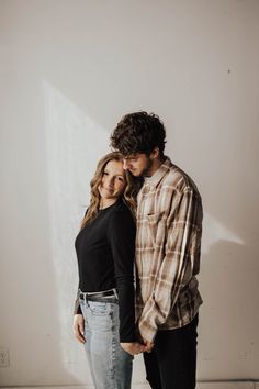 a man and woman standing next to each other with their arms around each other in front of a white wall