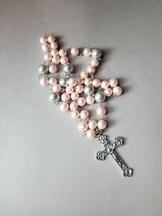 This Lutheran rosary has silver-toned findings and glass pearl beads in pink and gray. I used larger beads than I normally do on this one. It's really pretty. This rosary is hand-wired using silver-tone eye pins and my trusty little looper tool. The beads are connected by these loops. In the rosary itself, the small beads are 10mm pink glass pearls. The large beads are 12mm silver gray glass pearls. At the end of the stem is a silver-toned, budded metal crucifix. It measures 57mm x 35mm. 25.4 mm Silver Beaded Rosary For First Communion, Silver Pearl Rosary With 8mm Beads, Silver Pearl Rosary For First Communion, Silver Rosary With 8mm Beads And Crucifix, Handmade Silver Rosary With Crucifix, Handmade Pink Rosary With Cross Shape, Handmade Pink Rosary In Cross Shape, Handmade Pink Rosary With Cross, Handmade Pink Cross Rosary