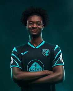 a soccer player poses for a portrait in front of a dark background with his arms crossed