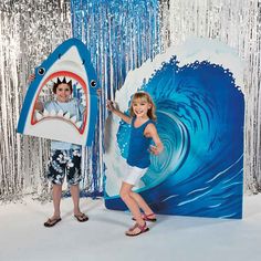 two children are standing in front of a backdrop with a shark and a man holding a surfboard