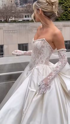 a woman in a white wedding dress is standing on a ledge looking at the city