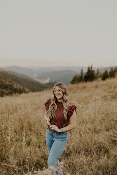 a woman standing in the middle of a field with her hands on her hips and smiling