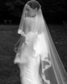 a woman in a wedding dress and veil walking through the grass with her hand on her hip