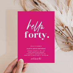 a person holding up a pink card with the words hello forty on it in front of feathers