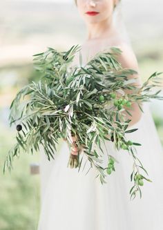 a woman in a wedding dress holding a bouquet of greenery