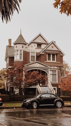 two cars are parked in front of a large house on a rainy day with autumn leaves