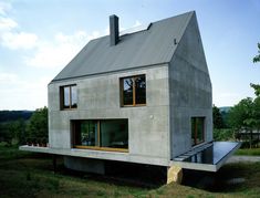 the house is made out of concrete and has two windows on each side, along with a deck