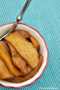 a bowl filled with baked apples sitting on top of a blue table cloth next to a spoon