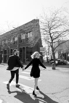 a man and woman walking across a street holding hands in the middle of the road