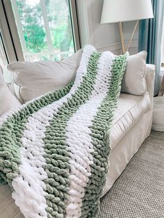 a green and white knitted blanket sitting on top of a couch next to a lamp