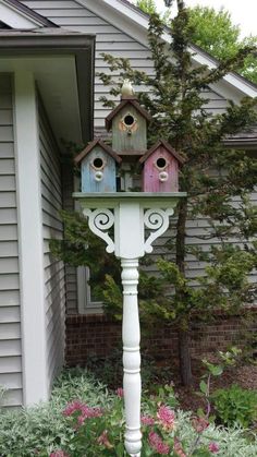 two bird houses on top of a white pole in front of a house with pink flowers