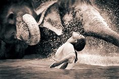 a boy is playing in the water with an elephant that has it's trunk over his head