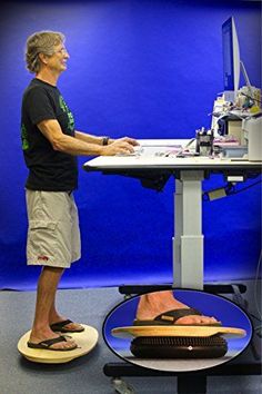 a man standing in front of a computer desk with his feet on the keyboard and foot rest