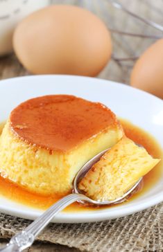 a white plate topped with cake covered in caramel sauce and two eggs behind it