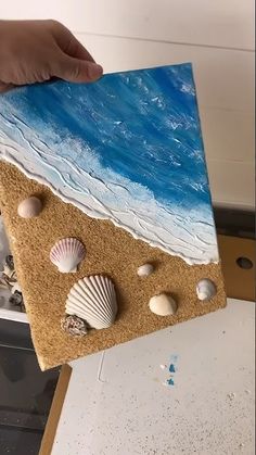 someone holding up a piece of art with seashells on it