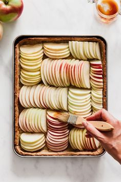 a person holding a wooden spoon over an apple tray with sliced apples on the side